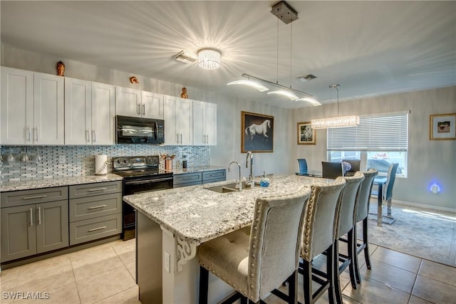 kitchen with black appliances, sink, light tile patterned floors, an island with sink, and decorative light fixtures