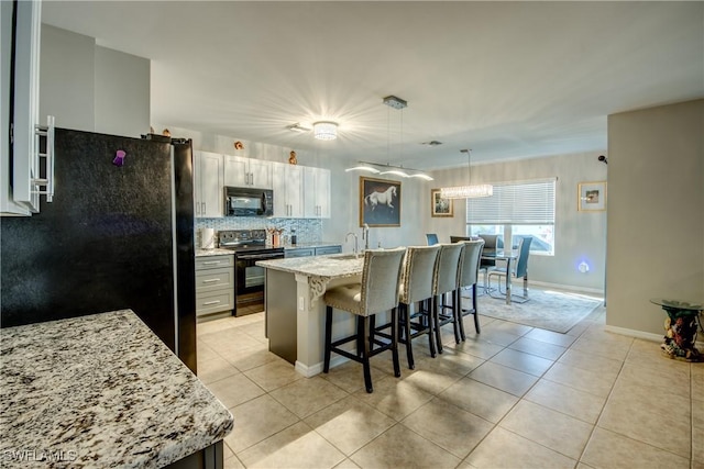 kitchen featuring a kitchen breakfast bar, refrigerator, hanging light fixtures, range with electric stovetop, and an island with sink