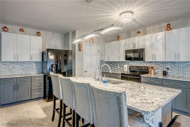 kitchen featuring an island with sink, hanging light fixtures, and black appliances