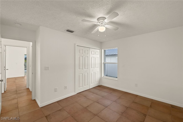 unfurnished bedroom with ceiling fan, tile patterned flooring, a closet, and a textured ceiling