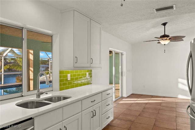 kitchen with sink, a textured ceiling, white cabinets, ceiling fan, and backsplash