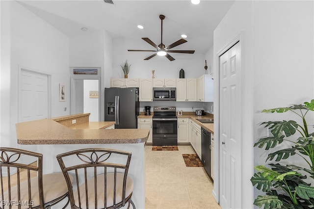 kitchen with white cabinets, ceiling fan, appliances with stainless steel finishes, light tile patterned flooring, and a kitchen bar