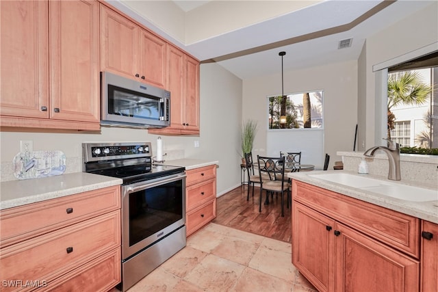 kitchen with light stone counters, sink, pendant lighting, and appliances with stainless steel finishes