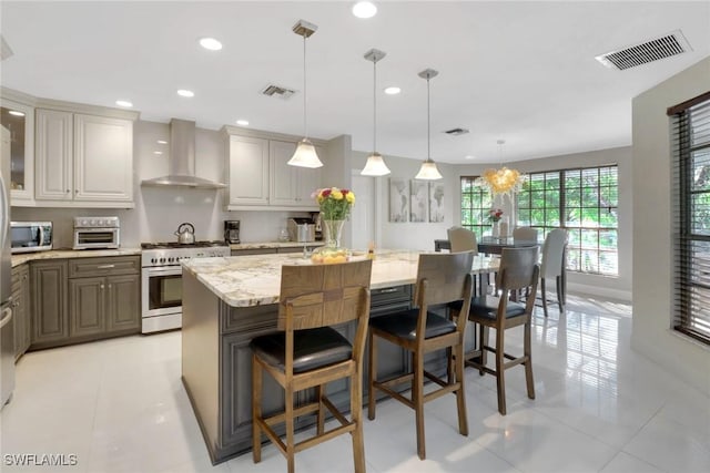 kitchen with decorative light fixtures, a kitchen bar, stainless steel appliances, wall chimney range hood, and a spacious island