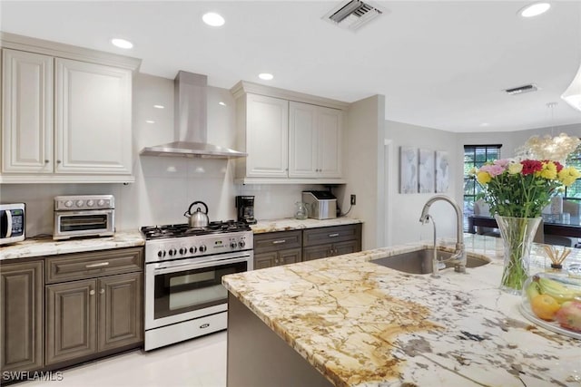 kitchen featuring appliances with stainless steel finishes, white cabinetry, sink, light stone countertops, and wall chimney range hood