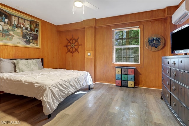 bedroom with a wall mounted air conditioner, wood-type flooring, wooden walls, and ceiling fan