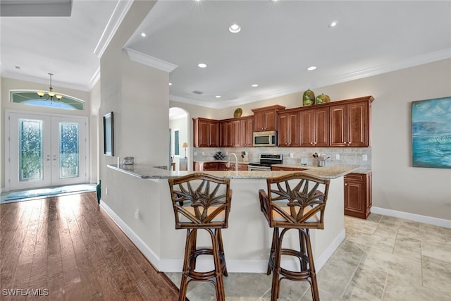 kitchen featuring french doors, stainless steel appliances, light stone counters, crown molding, and a breakfast bar area