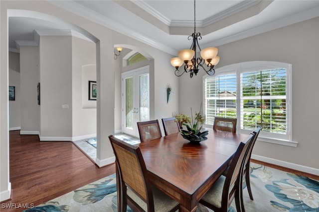 dining area with a notable chandelier, a healthy amount of sunlight, a raised ceiling, and crown molding