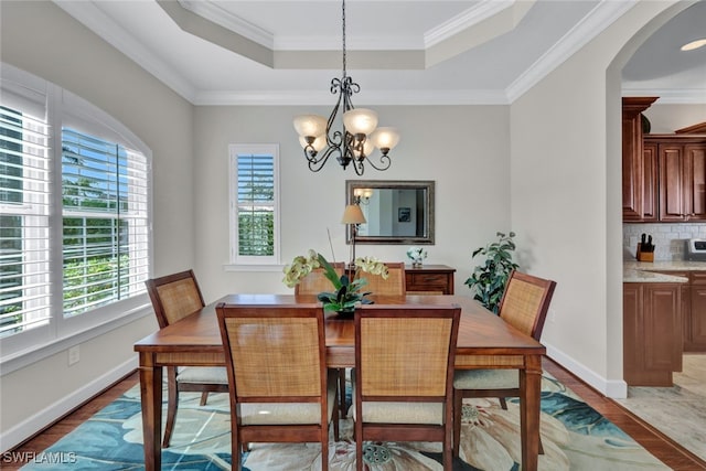 dining space with hardwood / wood-style flooring, a notable chandelier, ornamental molding, and a tray ceiling