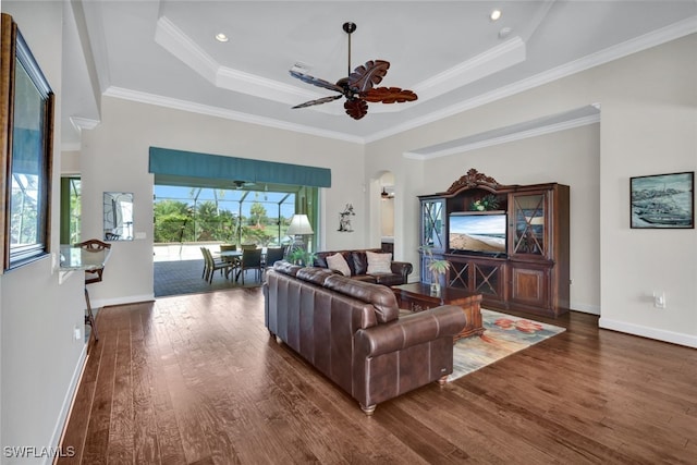 living room with a wealth of natural light, ceiling fan, dark wood-type flooring, crown molding, and a tray ceiling