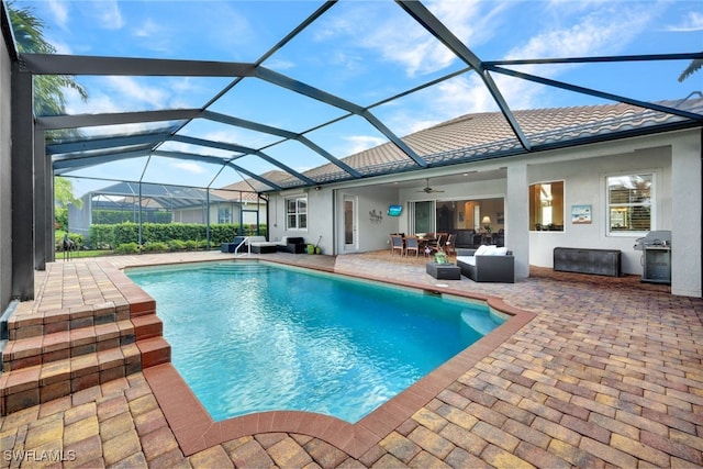 view of pool featuring glass enclosure, ceiling fan, a patio area, and grilling area