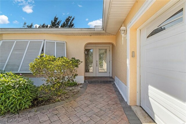 entrance to property with an attached garage, stucco siding, and french doors