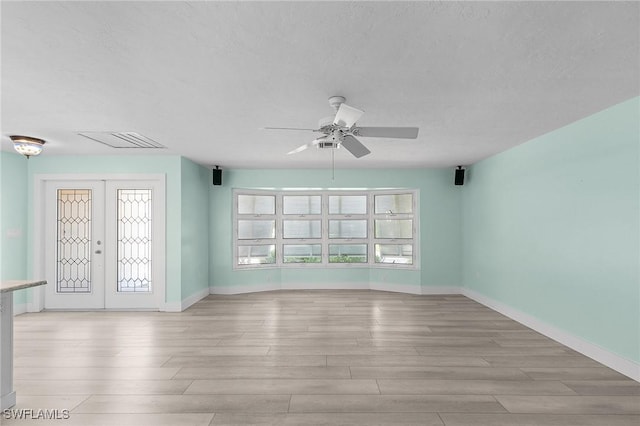 empty room with light wood finished floors, visible vents, baseboards, a textured ceiling, and french doors