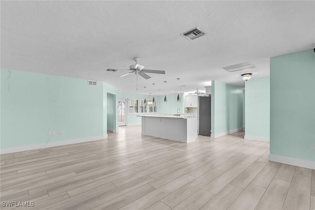 unfurnished living room featuring ceiling fan, baseboards, visible vents, and light wood-style floors