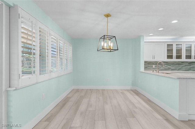 unfurnished dining area featuring light wood finished floors, recessed lighting, a sink, and baseboards