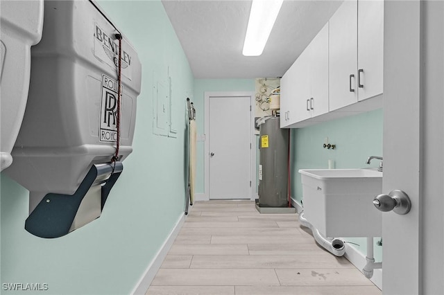 laundry area with water heater, cabinet space, wood tiled floor, a sink, and baseboards