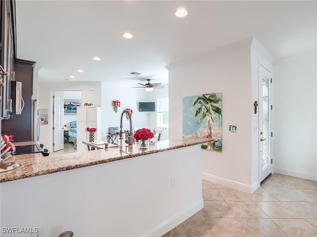 kitchen with dark brown cabinetry, light stone countertops, kitchen peninsula, and ceiling fan