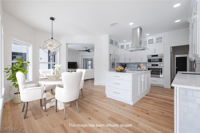 kitchen with appliances with stainless steel finishes, tasteful backsplash, island range hood, white cabinets, and hanging light fixtures