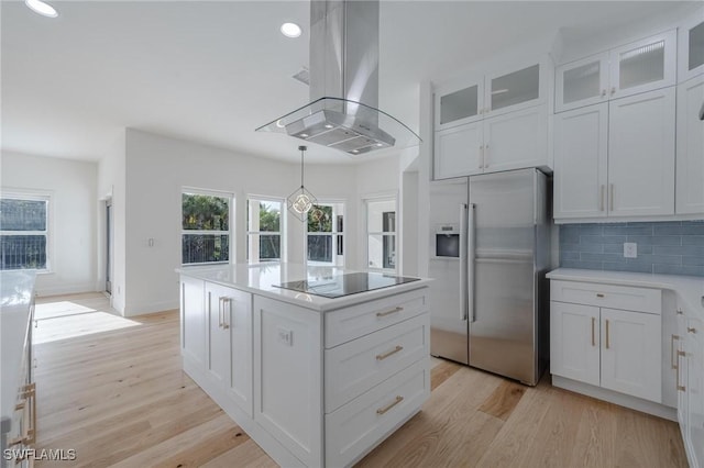 kitchen with white cabinetry, backsplash, island exhaust hood, stainless steel fridge, and black electric stovetop