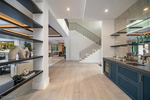 bar featuring light hardwood / wood-style floors, blue cabinets, plenty of natural light, and sink