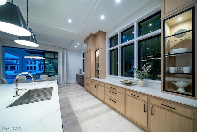 kitchen with light stone counters, sink, decorative light fixtures, and light brown cabinets