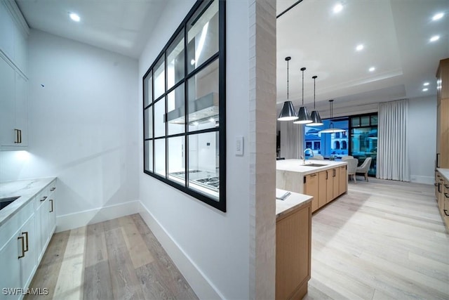 kitchen with light wood-type flooring, light stone counters, sink, light brown cabinets, and decorative light fixtures