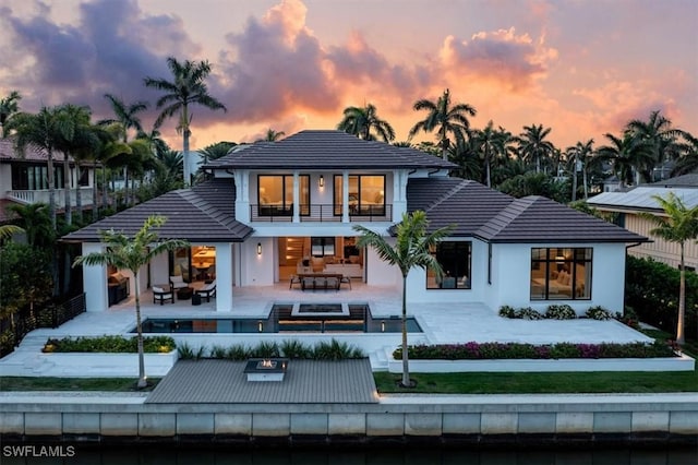 back house at dusk with an outdoor hangout area, a balcony, and a patio