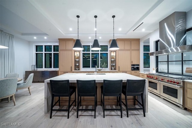 kitchen featuring double oven range, a large island with sink, sink, wall chimney exhaust hood, and light brown cabinetry