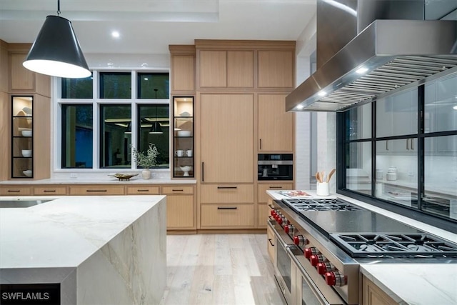 kitchen featuring light brown cabinets, high end range, wall chimney range hood, decorative light fixtures, and light stone counters