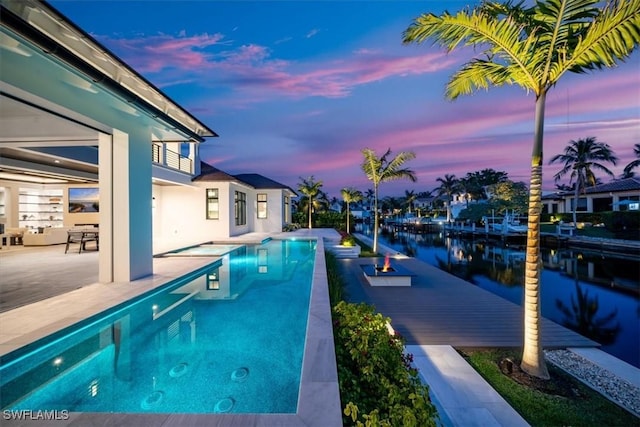 pool at dusk with a water view, a patio, and an outdoor fire pit