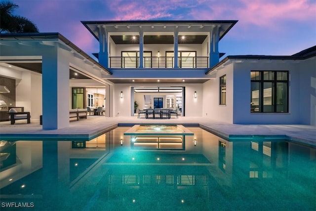 back house at dusk with a pool with hot tub, a patio area, a balcony, and an outdoor living space