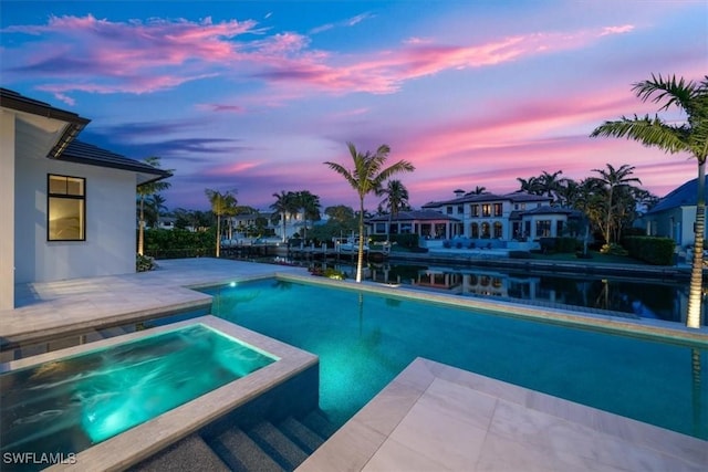 pool at dusk with a patio area, an in ground hot tub, and a water view