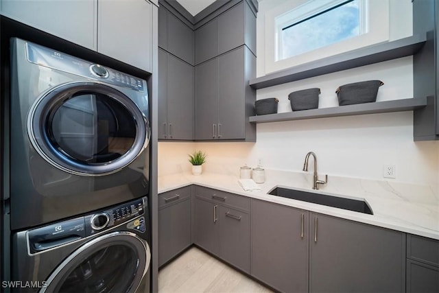 washroom with sink, cabinets, stacked washer / drying machine, and light wood-type flooring