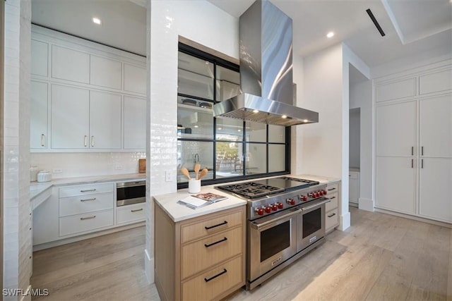 kitchen with light brown cabinets, double oven range, white cabinets, light hardwood / wood-style flooring, and island range hood