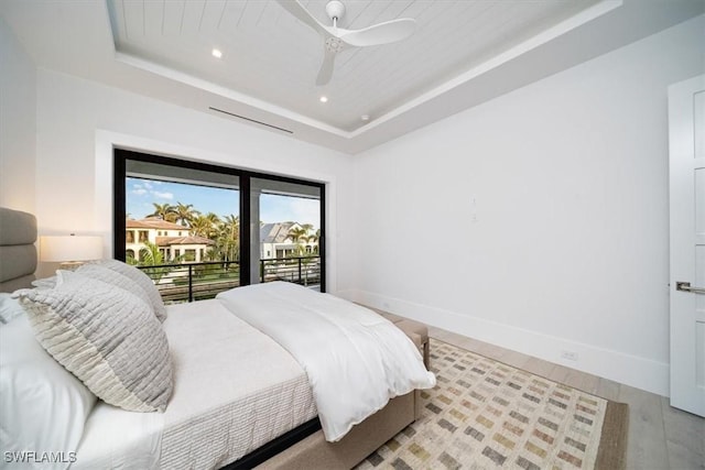 bedroom featuring access to outside, ceiling fan, a tray ceiling, and light wood-type flooring