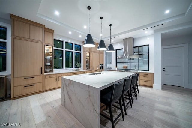 kitchen with light stone countertops, a spacious island, exhaust hood, decorative light fixtures, and light hardwood / wood-style floors