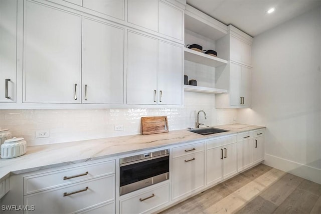 kitchen featuring backsplash, white cabinets, sink, light hardwood / wood-style flooring, and light stone counters