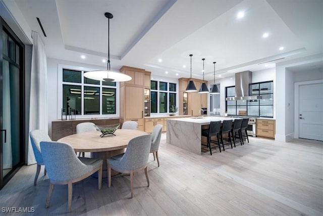 dining area with a raised ceiling, sink, and light wood-type flooring