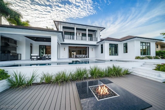 rear view of property with a balcony, an outdoor fire pit, and a pool side deck