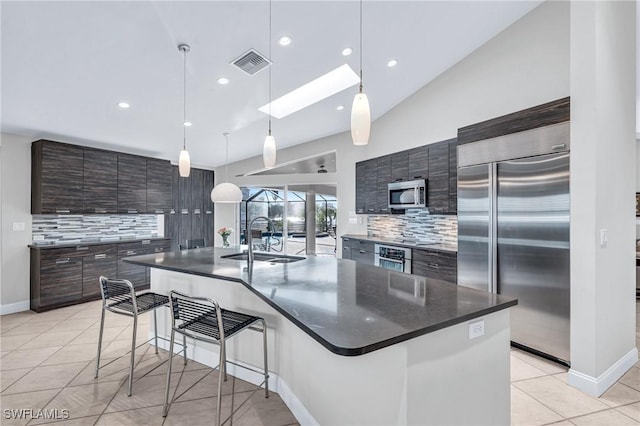 kitchen with sink, hanging light fixtures, an island with sink, decorative backsplash, and appliances with stainless steel finishes