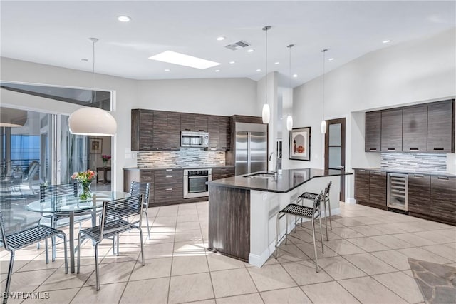 kitchen with appliances with stainless steel finishes, a skylight, tasteful backsplash, pendant lighting, and an island with sink