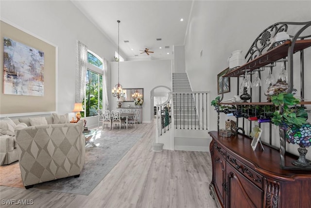 entryway featuring ceiling fan with notable chandelier, light hardwood / wood-style floors, and a towering ceiling