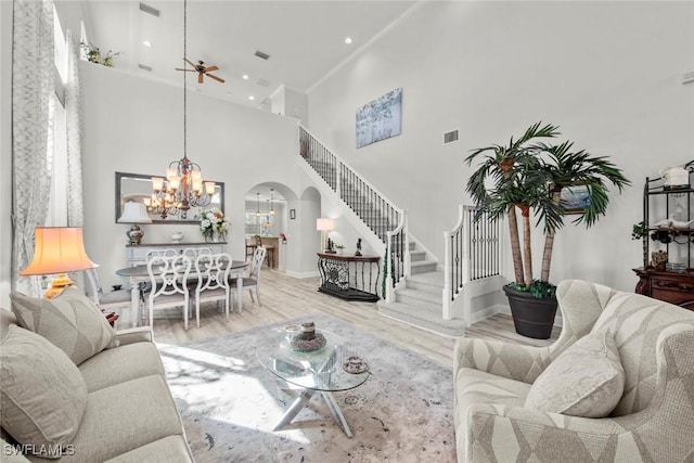 living room with wood-type flooring, ceiling fan with notable chandelier, and a high ceiling