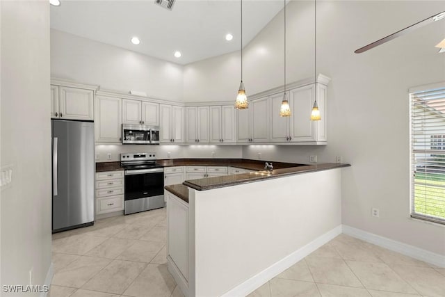 kitchen featuring kitchen peninsula, a towering ceiling, stainless steel appliances, and white cabinets