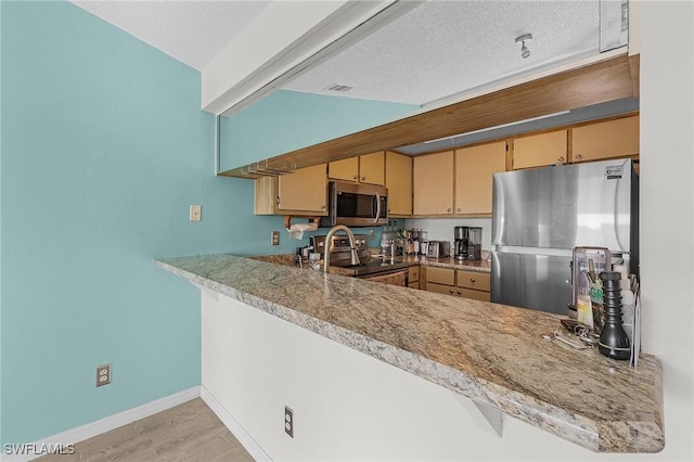 kitchen with kitchen peninsula, appliances with stainless steel finishes, a textured ceiling, vaulted ceiling, and light hardwood / wood-style flooring