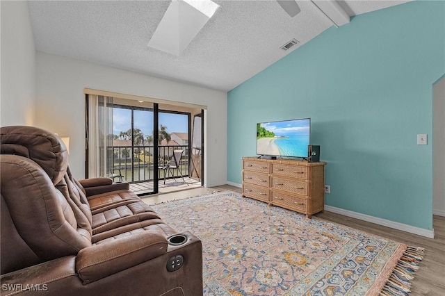 living room featuring hardwood / wood-style floors, ceiling fan, lofted ceiling with skylight, and a textured ceiling