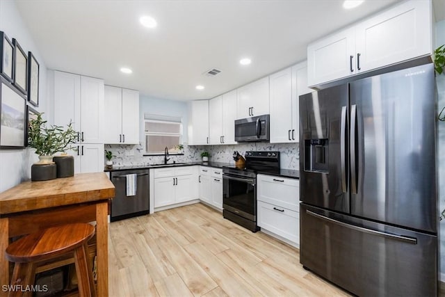 kitchen featuring backsplash, white cabinets, sink, appliances with stainless steel finishes, and light hardwood / wood-style floors