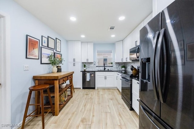 kitchen with tasteful backsplash, sink, black appliances, light hardwood / wood-style flooring, and white cabinets