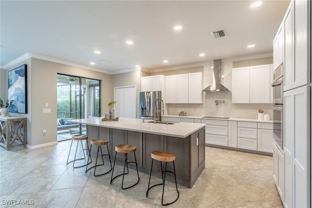 kitchen featuring white cabinets, a breakfast bar, wall chimney range hood, and a kitchen island with sink