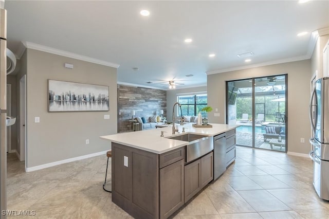 kitchen with ceiling fan, sink, stainless steel appliances, an island with sink, and ornamental molding